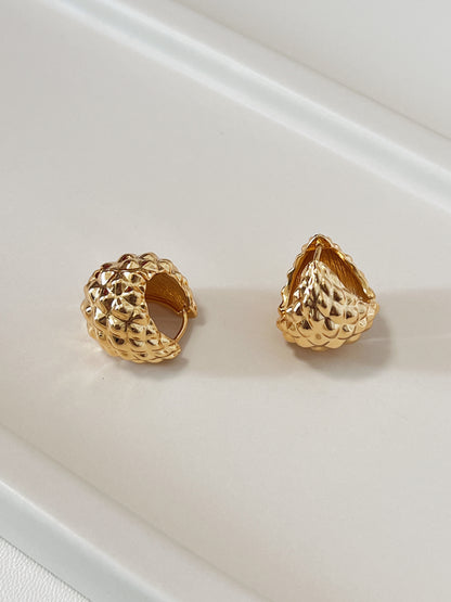 Two gold textured hoop earrings on a light beige surface