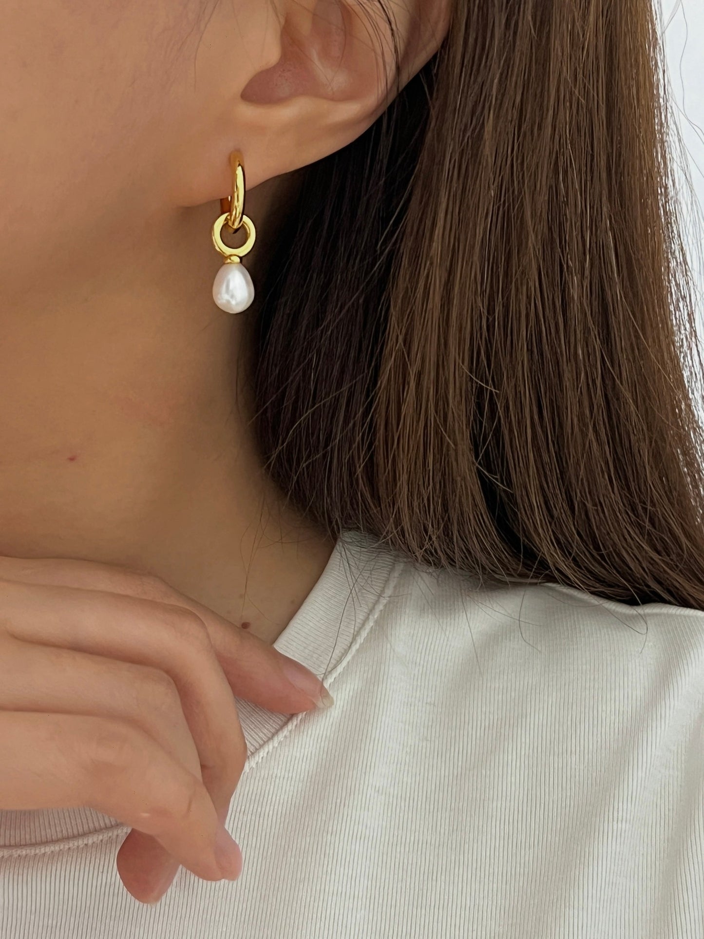 A woman wearing a dainty gold dangle pearl earrings, pairs with white outfit for a clean elegant look