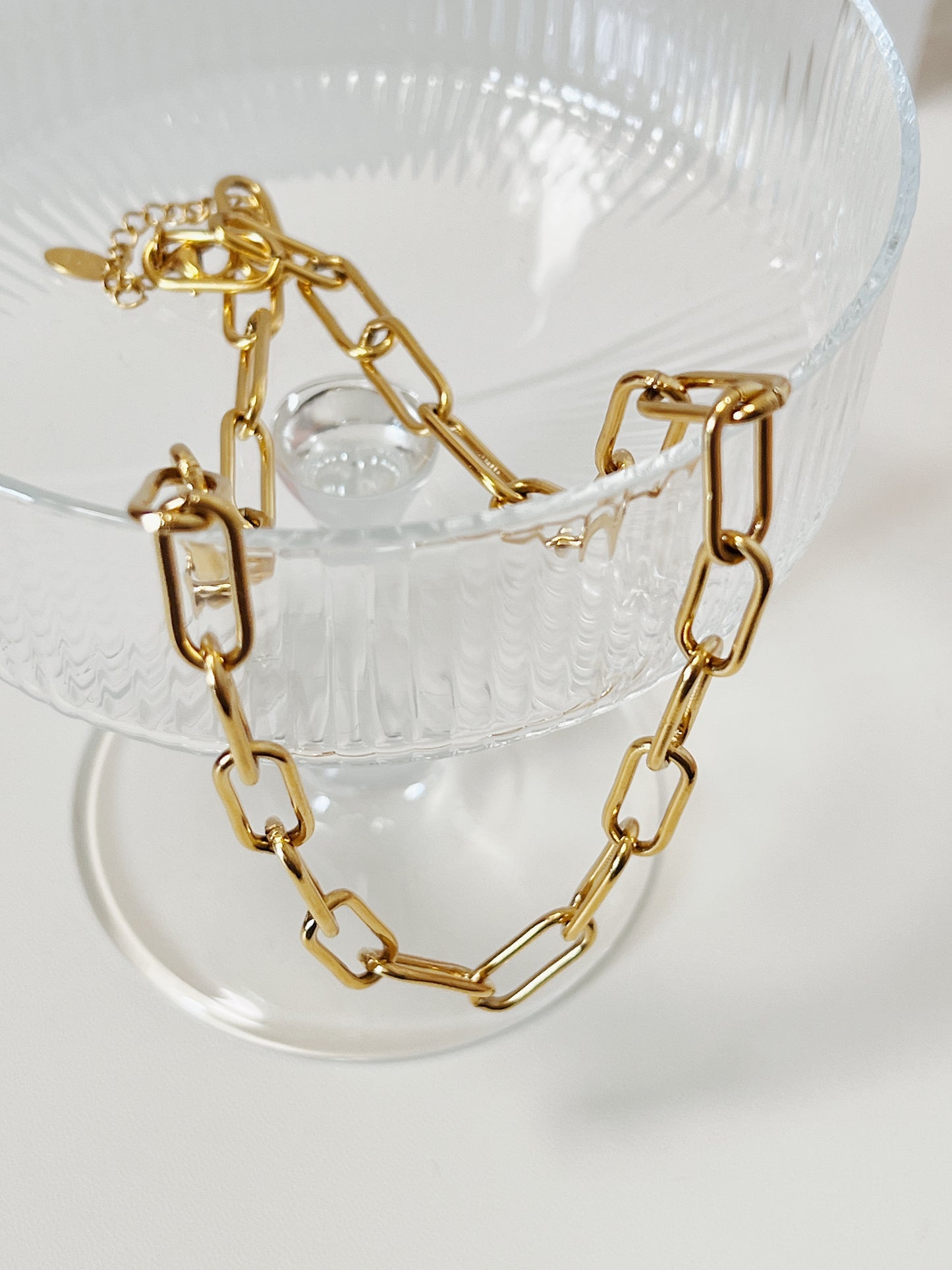 Gold link chain necklace on a clear glass stand with a white background