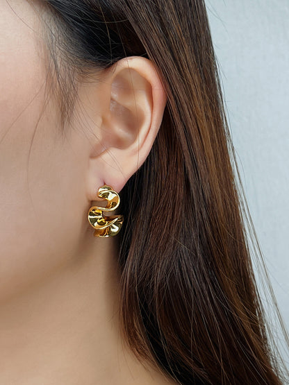 Gold wavy earrings worn by a person with a neutral background