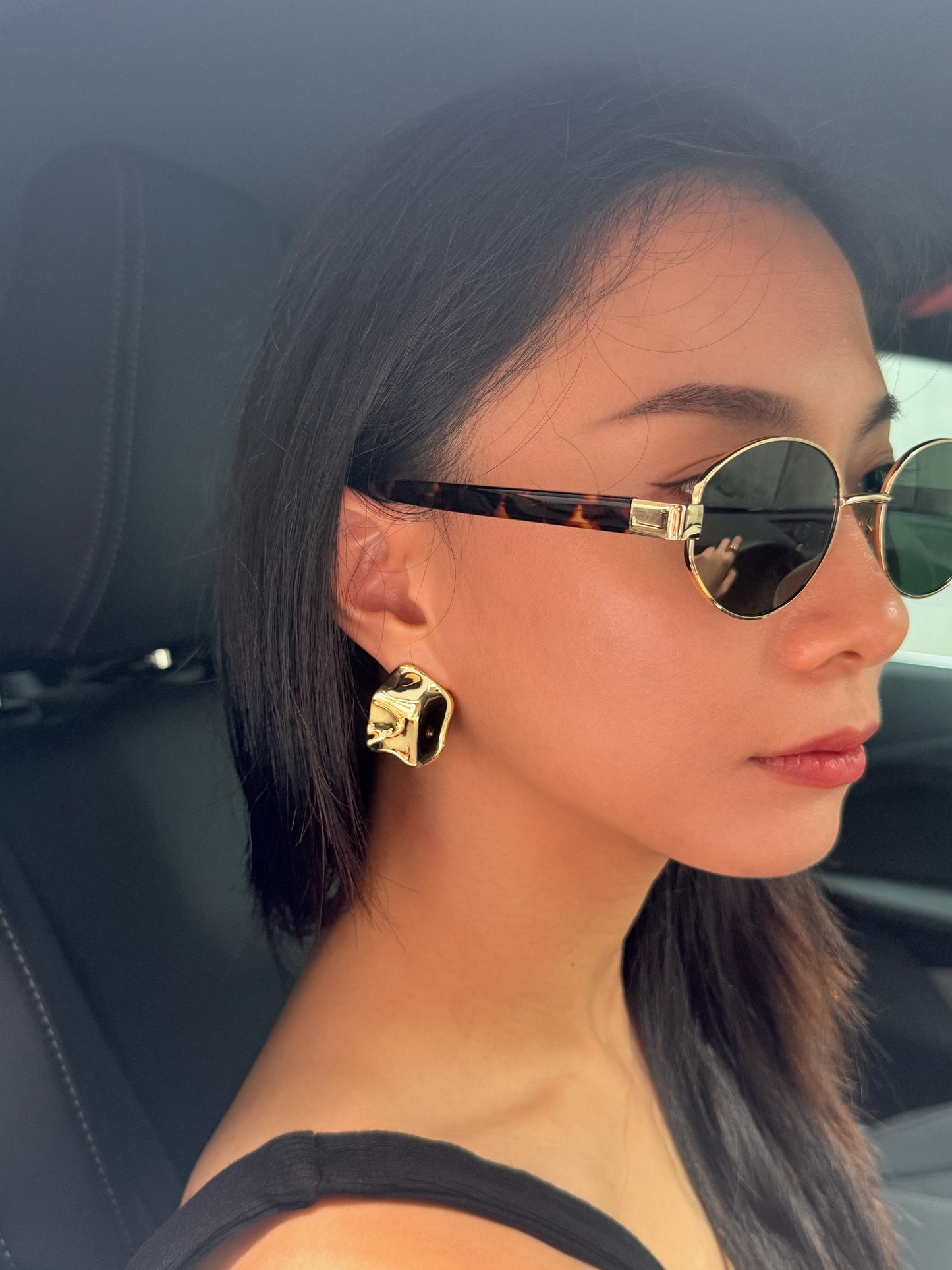 Woman wearing gold sunglasses and earrings inside a car