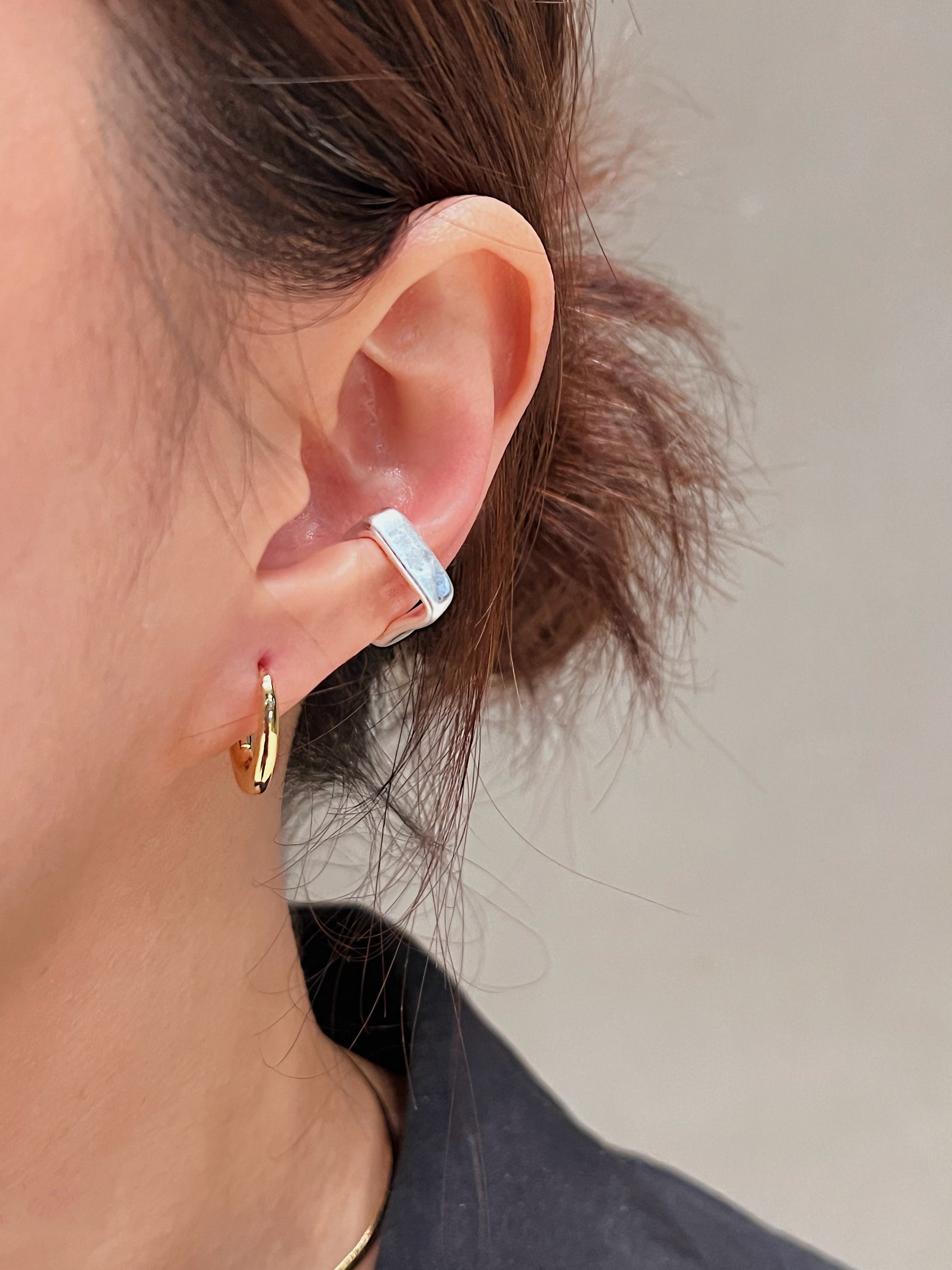 Close-up of an ear wearing a small silver cuff earring with a neutral background