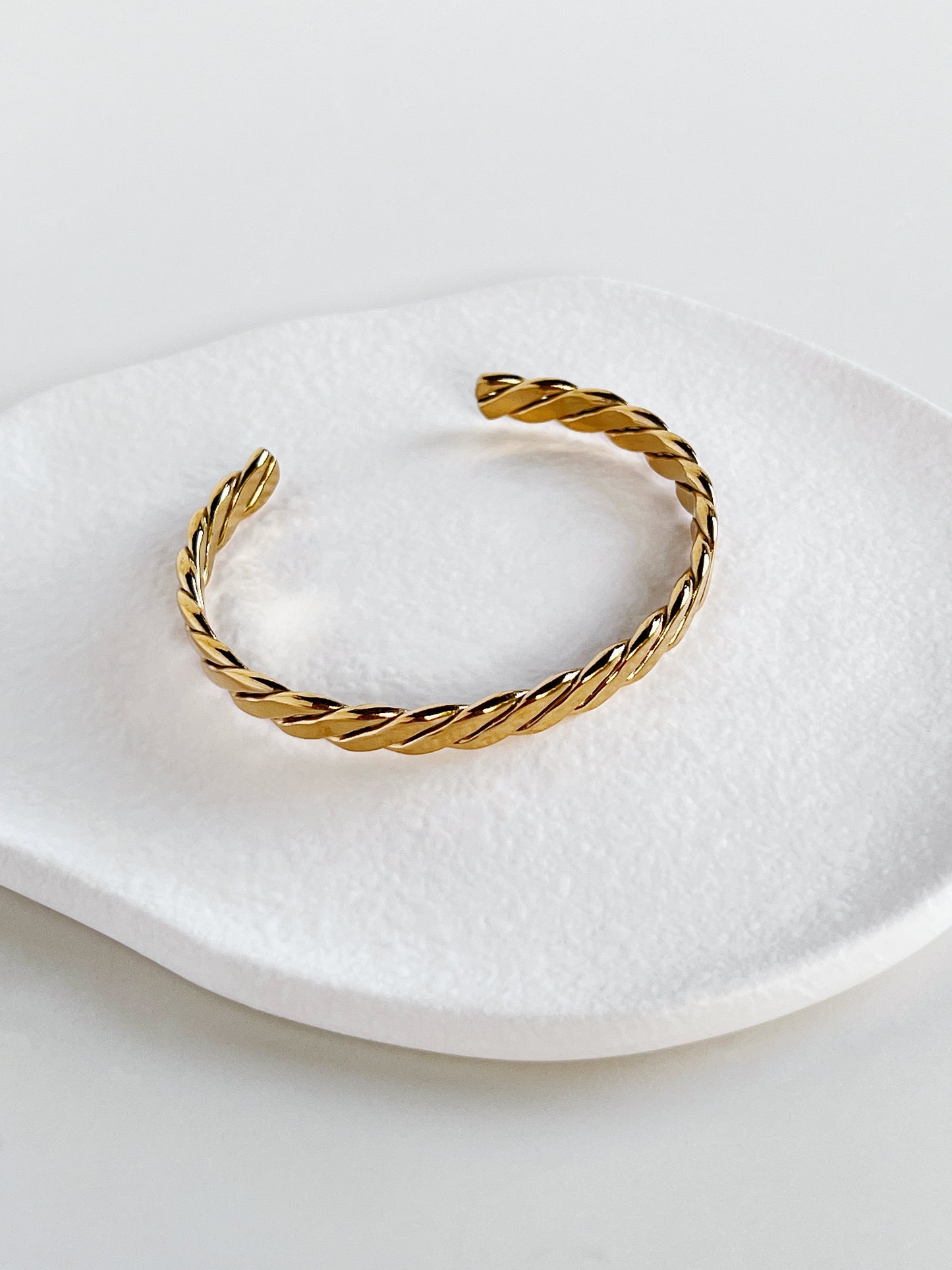 Gold braided bracelet on a white dish with a white background