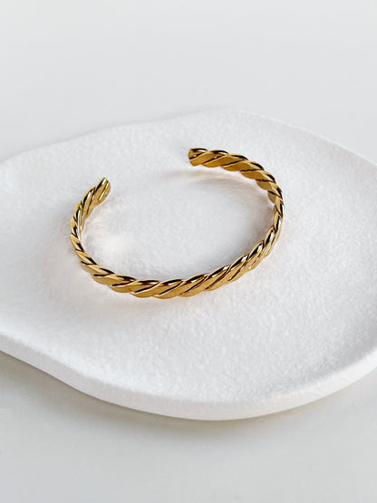 Gold braided bracelet on a white dish with a white background