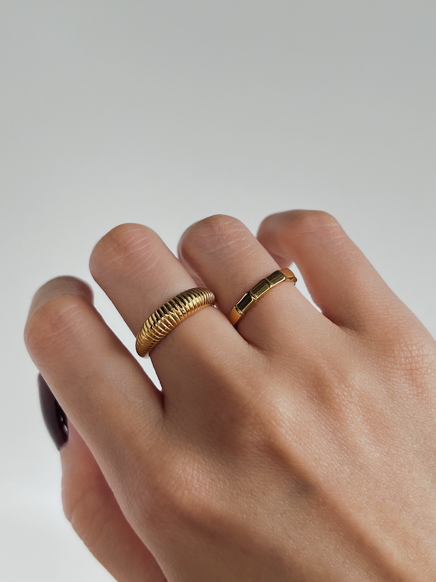 Hand wearing two gold rings on a plain background