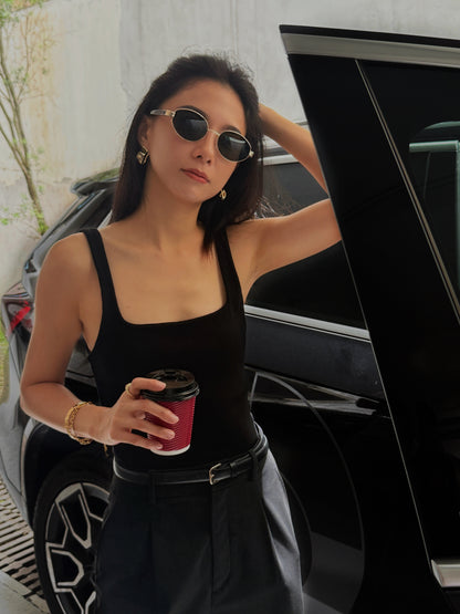 Woman in black outfit holding a coffee cup, standing next to a car.