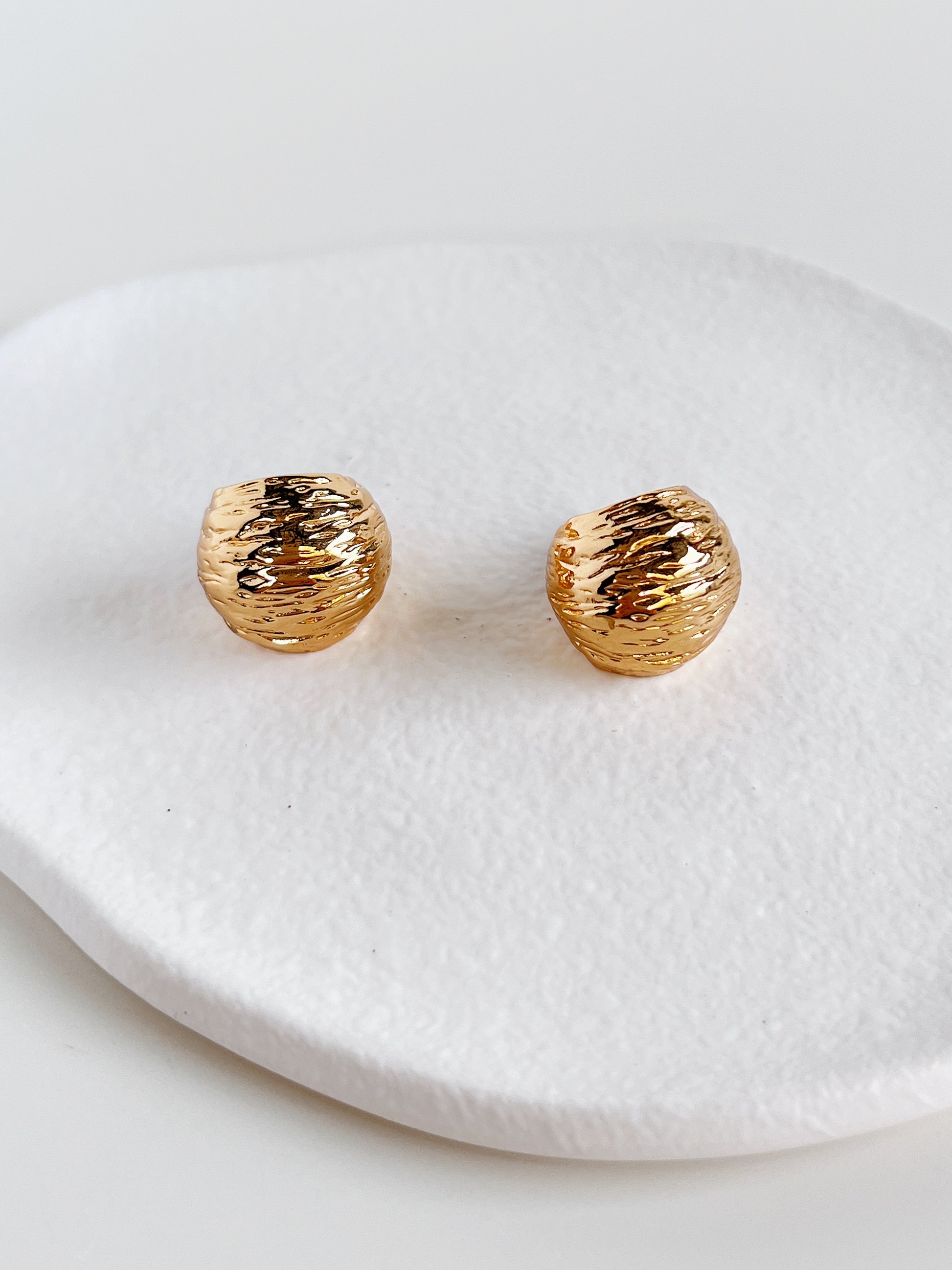 Gold textured earrings on a white dish
