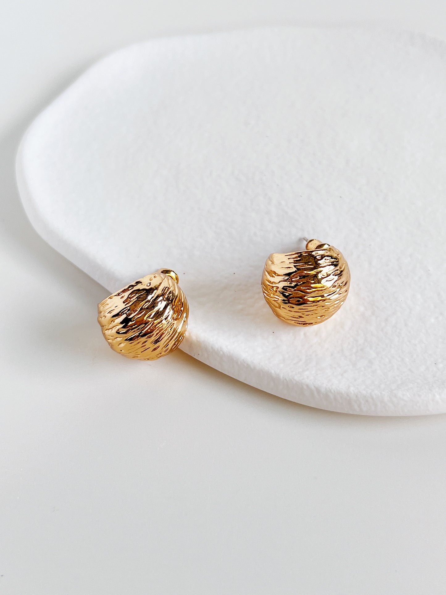 Gold earrings on a white ceramic surface
