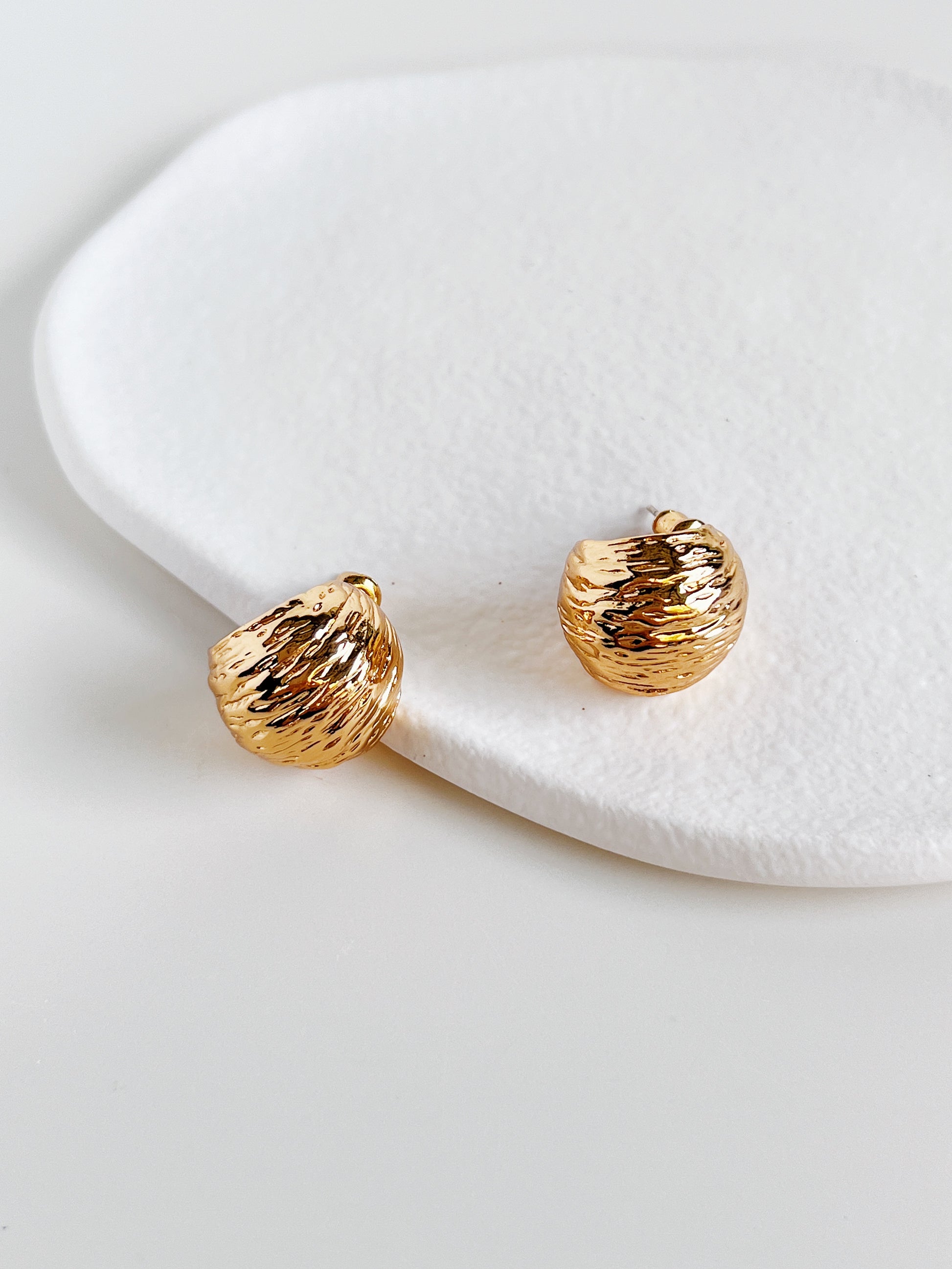 Gold earrings on a white ceramic surface