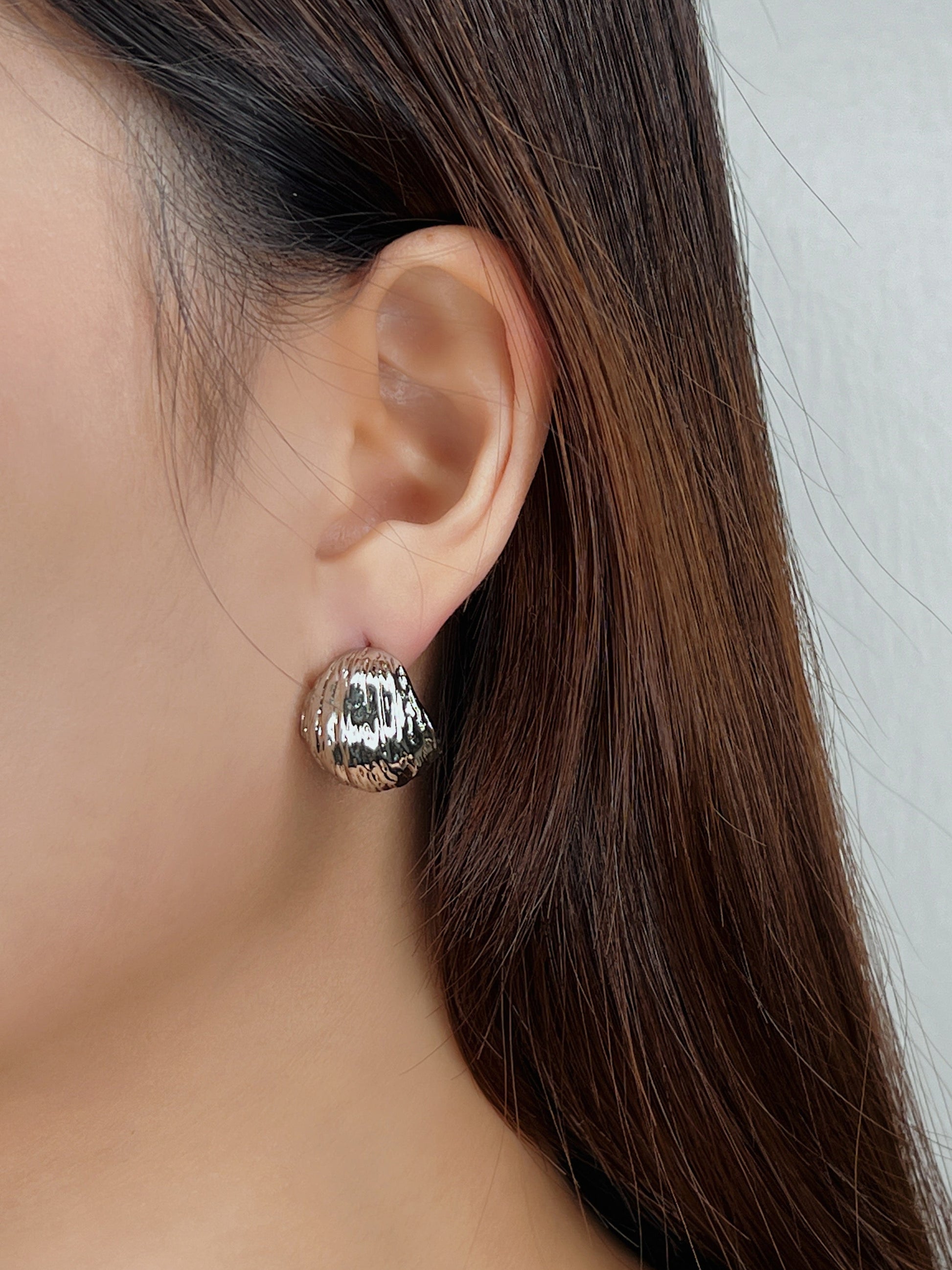 Close-up of a person wearing a silver earring with a textured design.