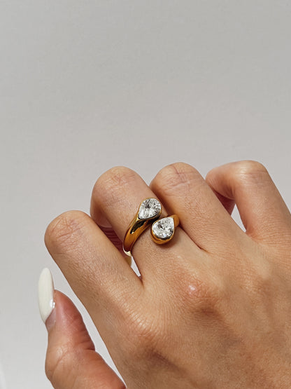 Hand wearing a gold ring with two diamonds on a neutral background