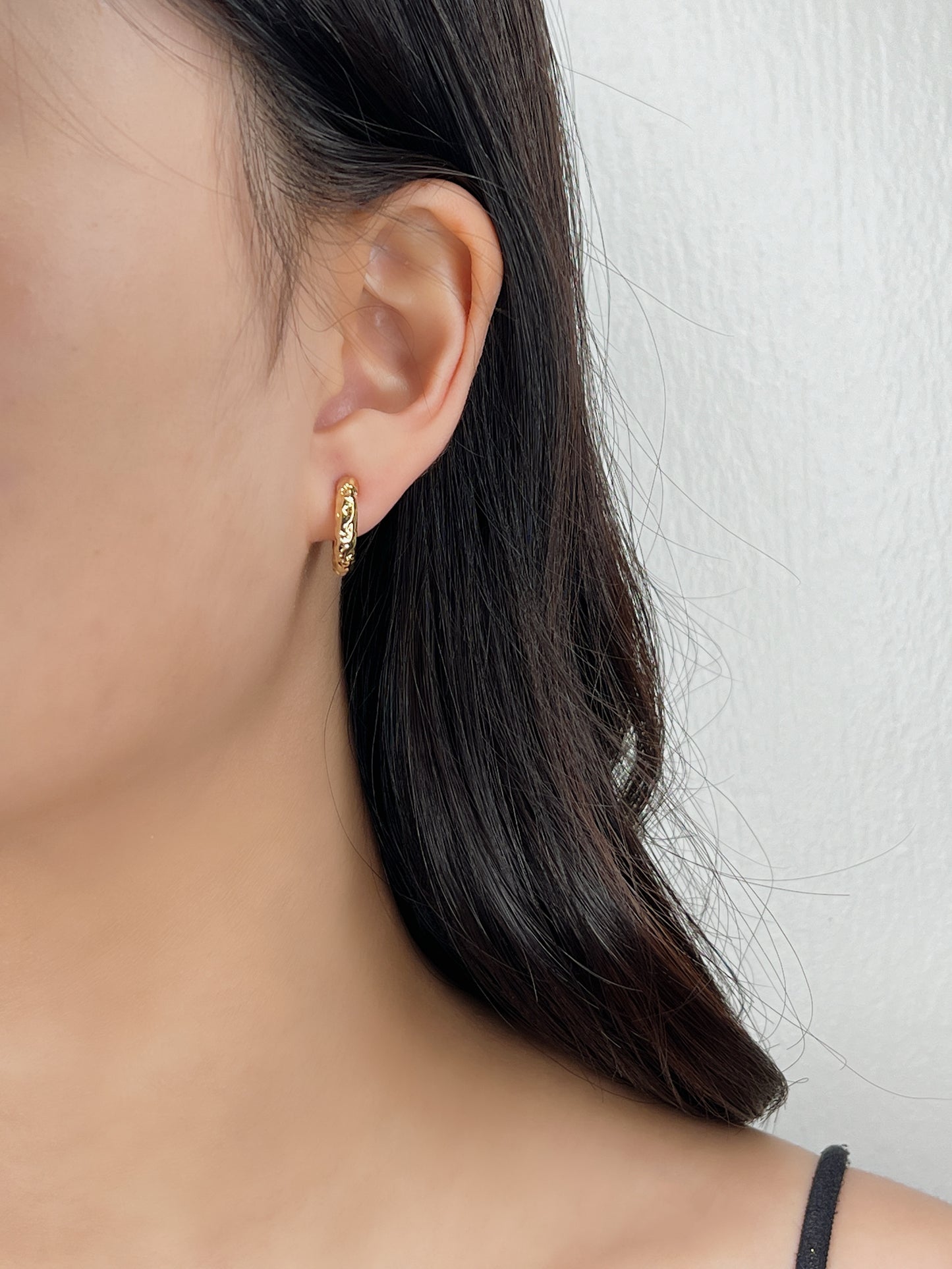 Close-up of a person wearing a gold huggie hoop earring against a neutral background