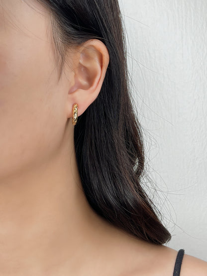 Close-up of a person wearing a gold huggie hoop earring against a neutral background