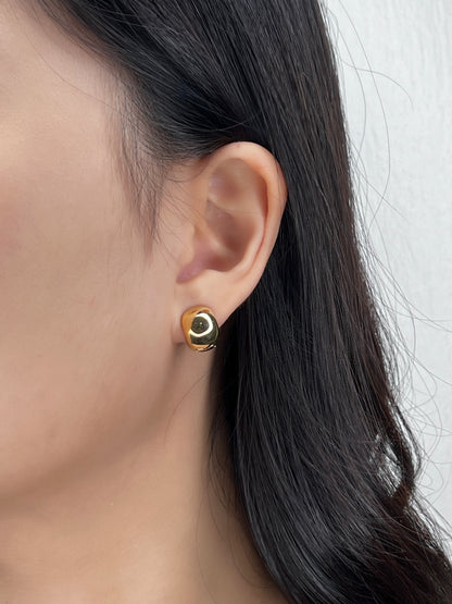 Close-up of a person wearing a classicc gold huggie earring with a white background