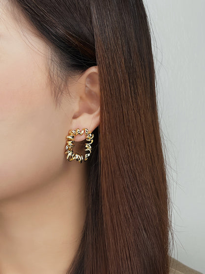 Gold curly earrings worn by a person with long brown hair against a plain background