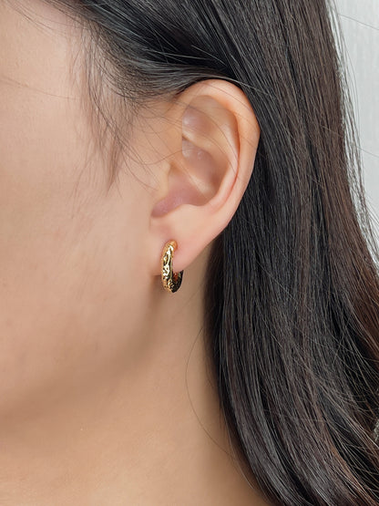 Close-up of a person wearing gold hammered huggie hoop earrings with a neutral background
