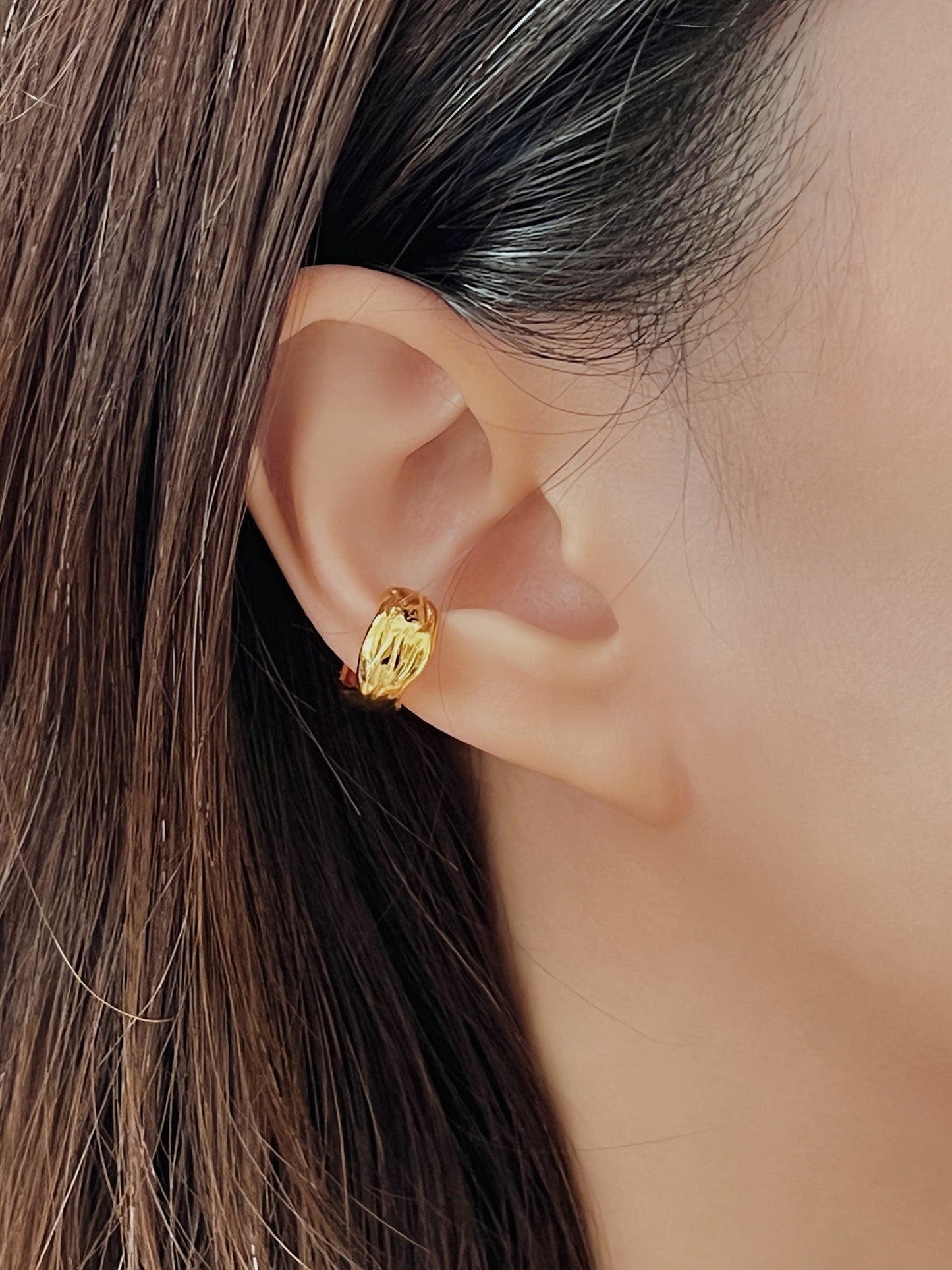Gold textured cuff earring worn by a person with brown hair.