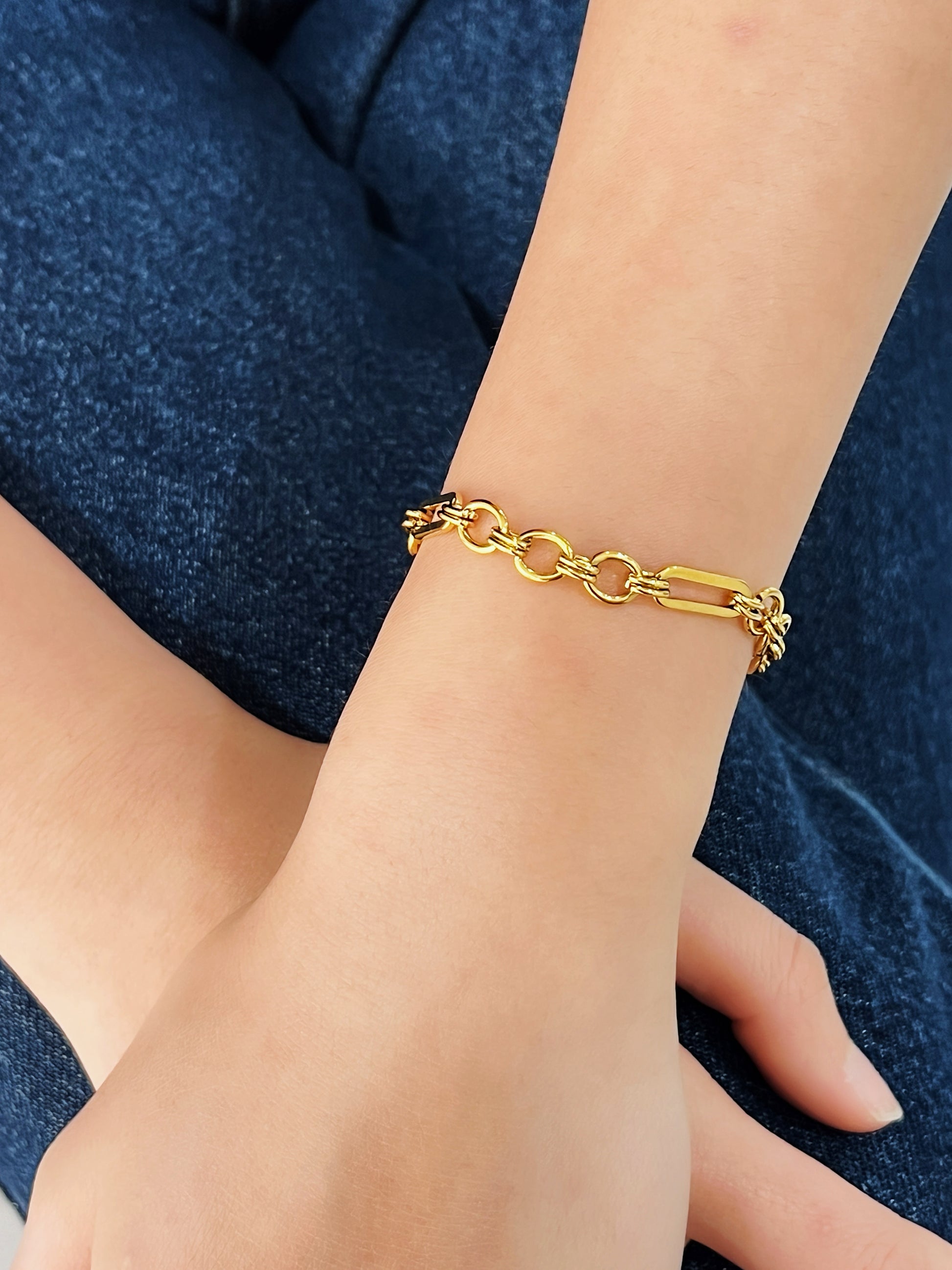Gold chain bracelet on a wrist against a blue denim background