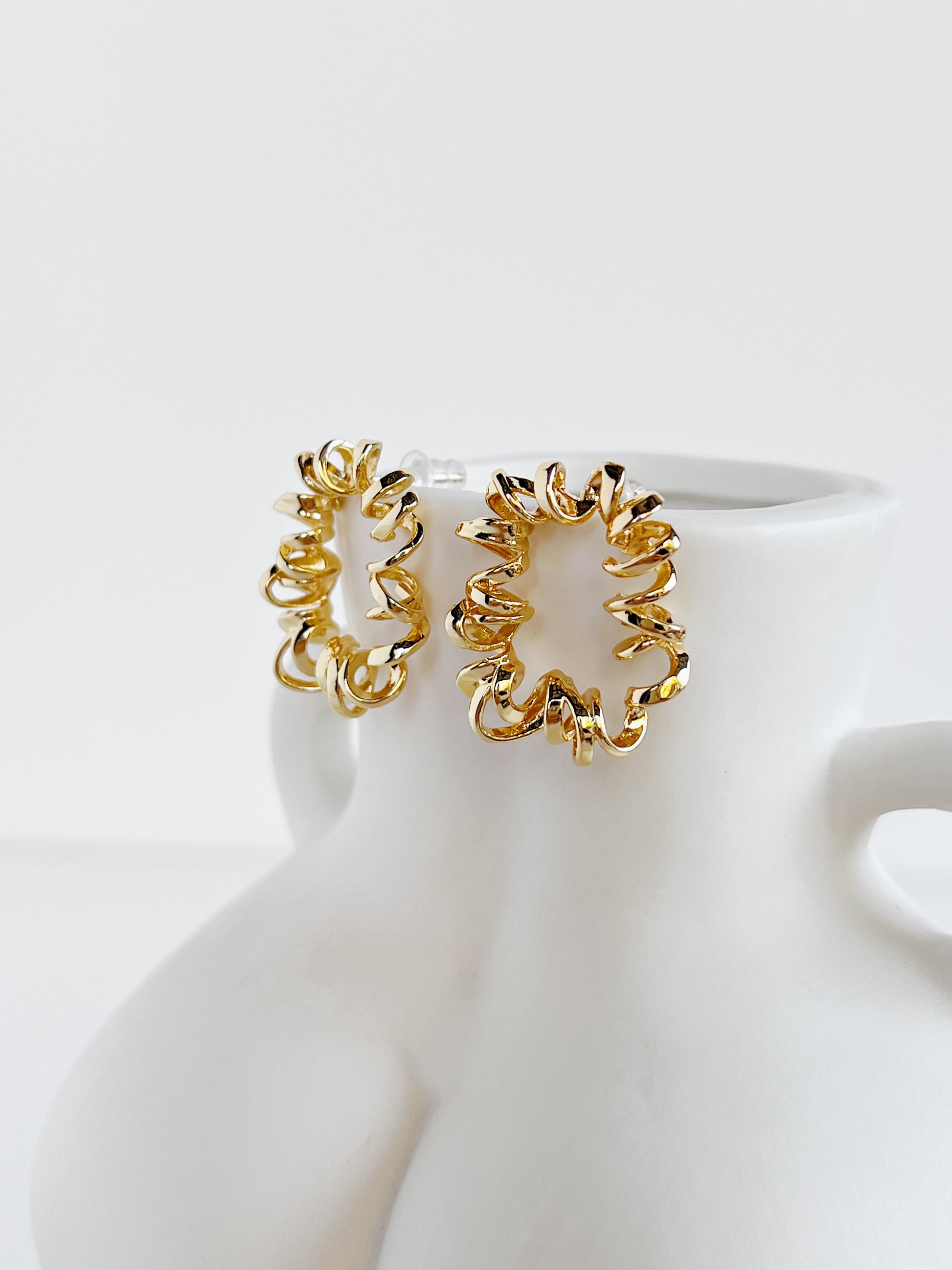 Gold wire stud earrings on a white mannequin bust against a white background