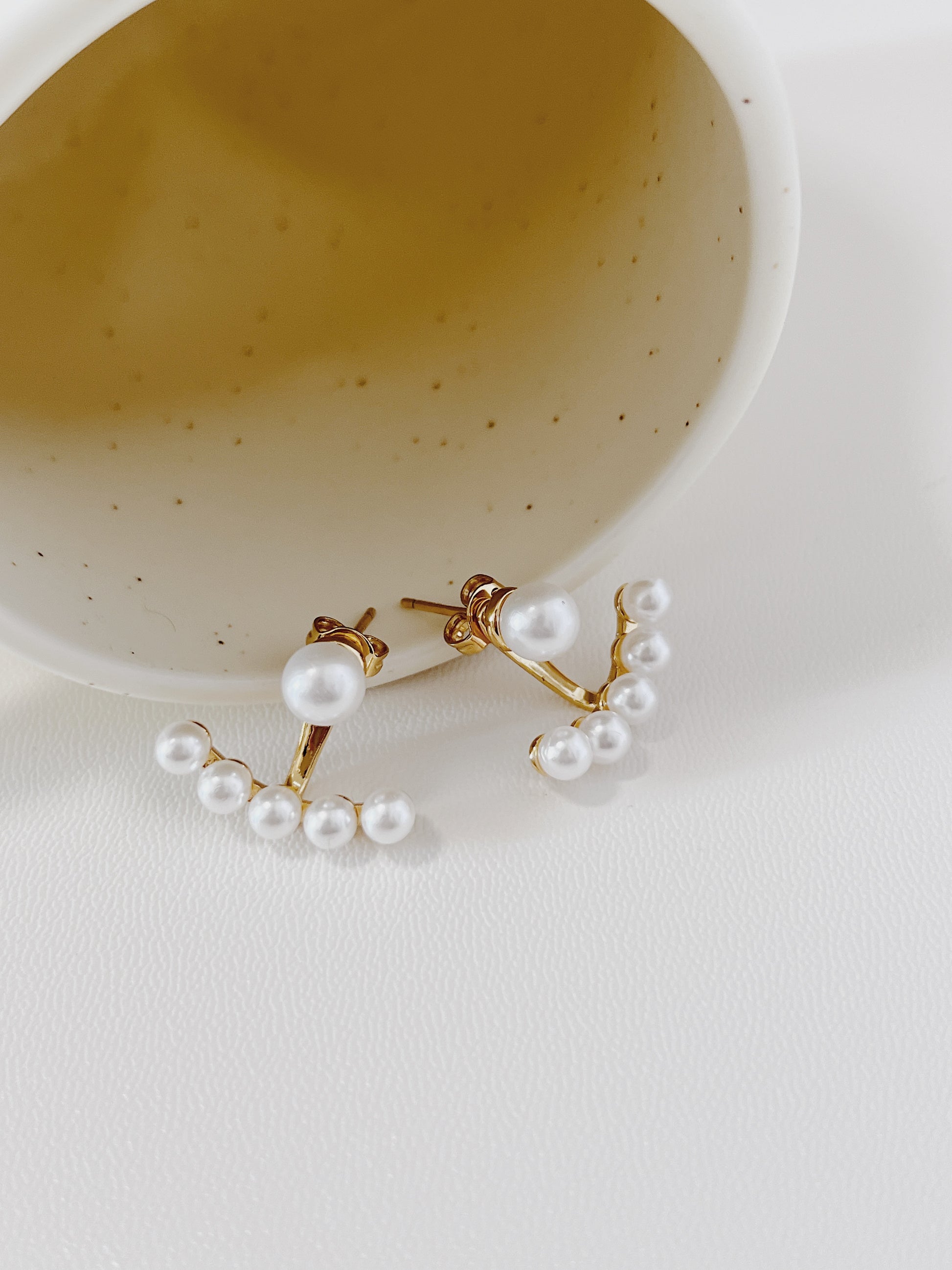 Pearl ear jacket earrings on a white surface with a speckled bowl in the background