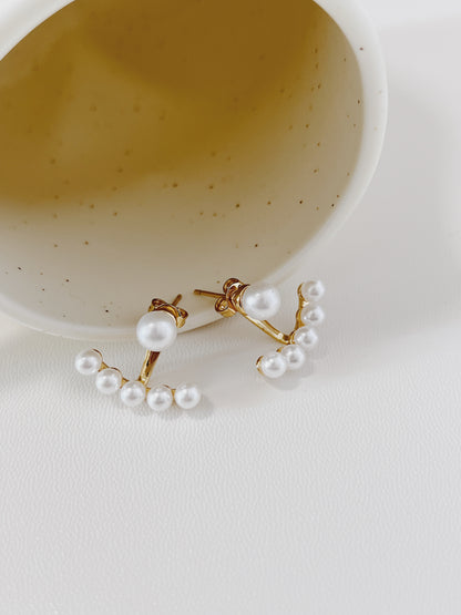Pearl ear jacket earrings on a white surface with a speckled bowl in the background
