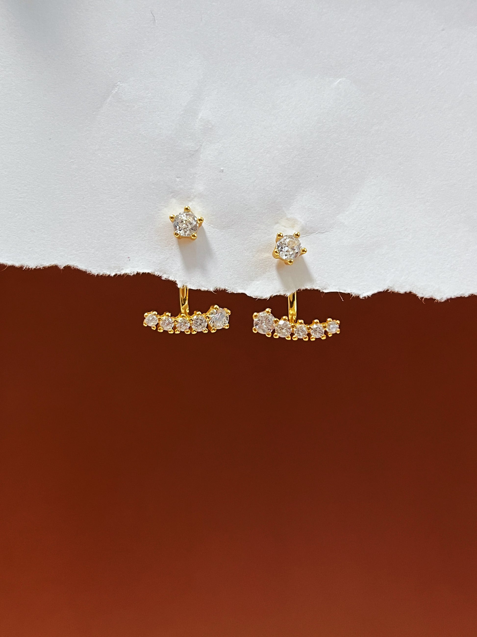 Gold diamond ear jacket earrings with gemstones on a white and brown background