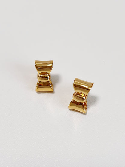 Gold bow-shaped earrings on a light gray background