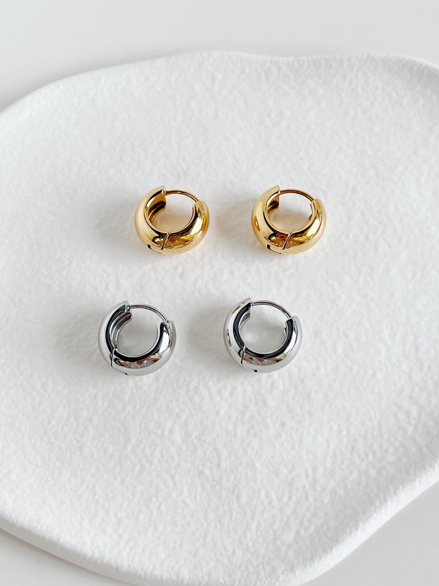 Set of gold and silver chunky huggie hoop earrings on a white ceramic dish