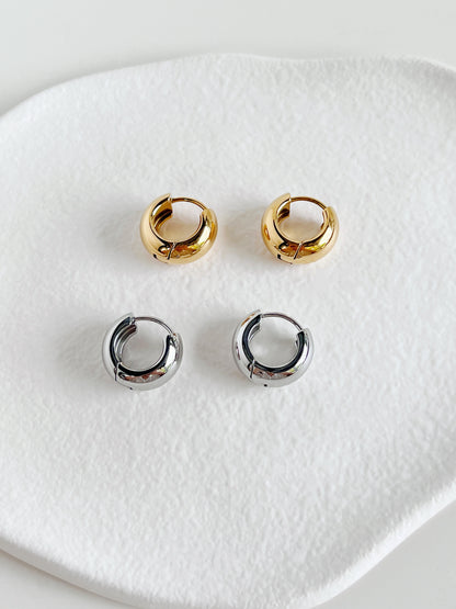 Set of gold and silver chunky huggie hoop earrings on a white ceramic dish