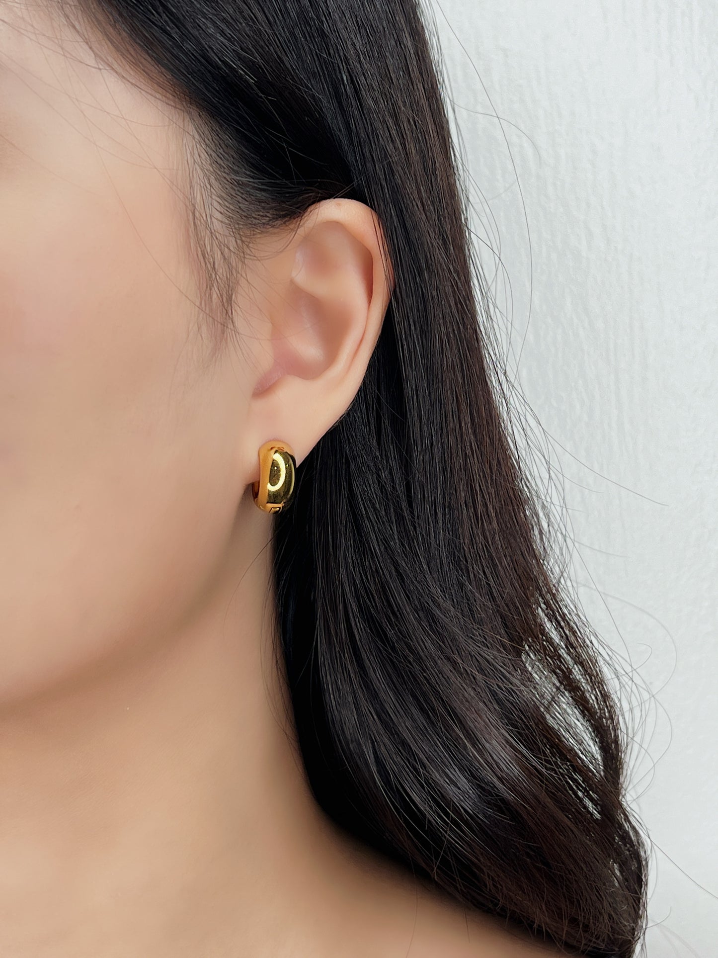 Gold huggie earring worn by a person with dark hair on a white background
