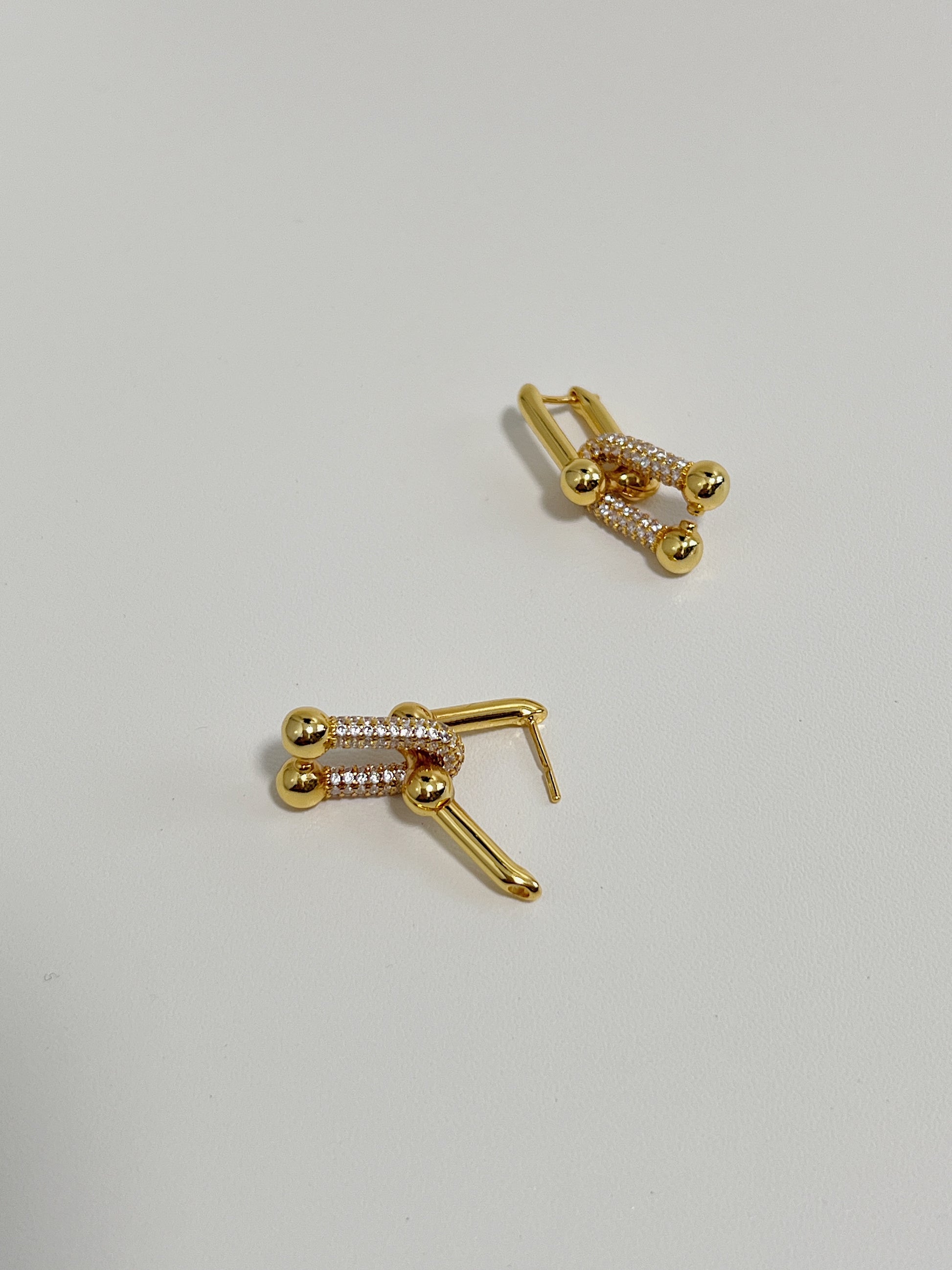 Detailed view of a gold link earrings featuring diamonds and interlocking design with a soft-focus white background.