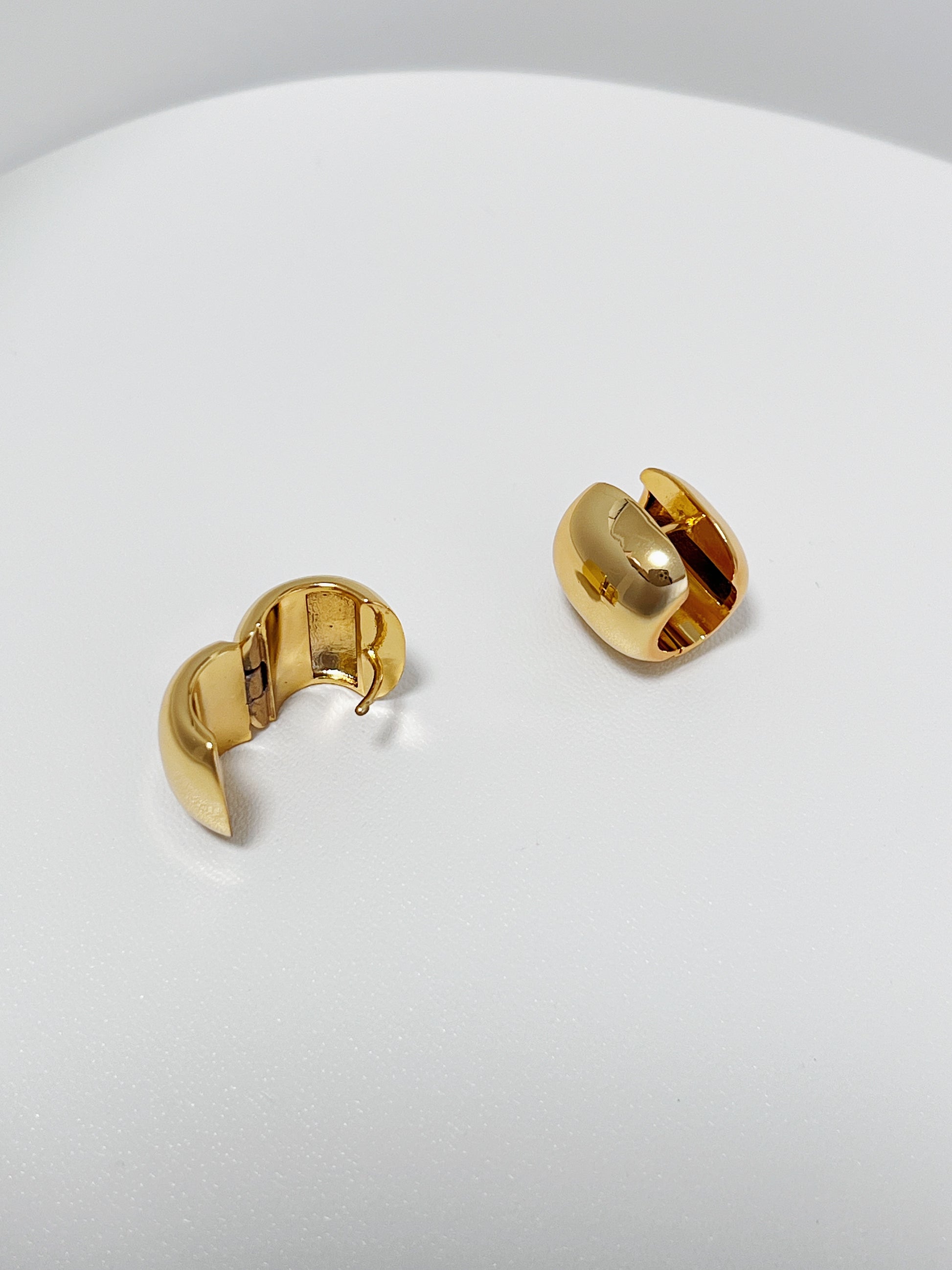 Gold wide hoop earrings on a white surface