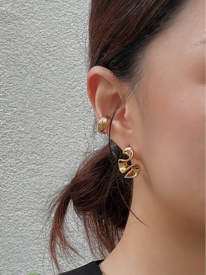 Close-up of a person wearing gold wavy earrings against a neutral background