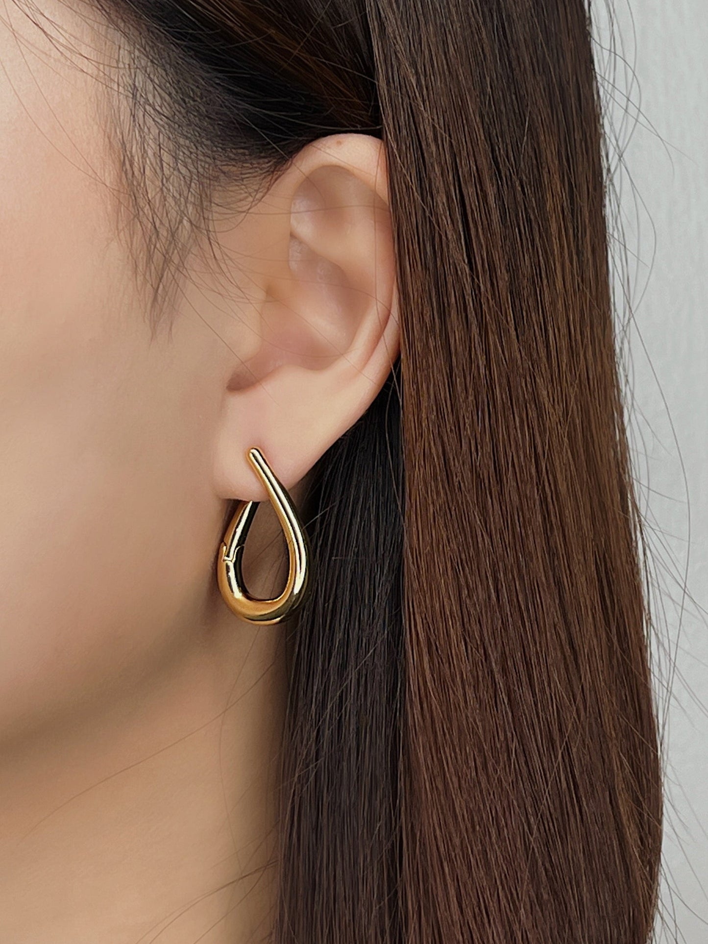 Close-up of a person wearing a gold hoop earring with a neutral background