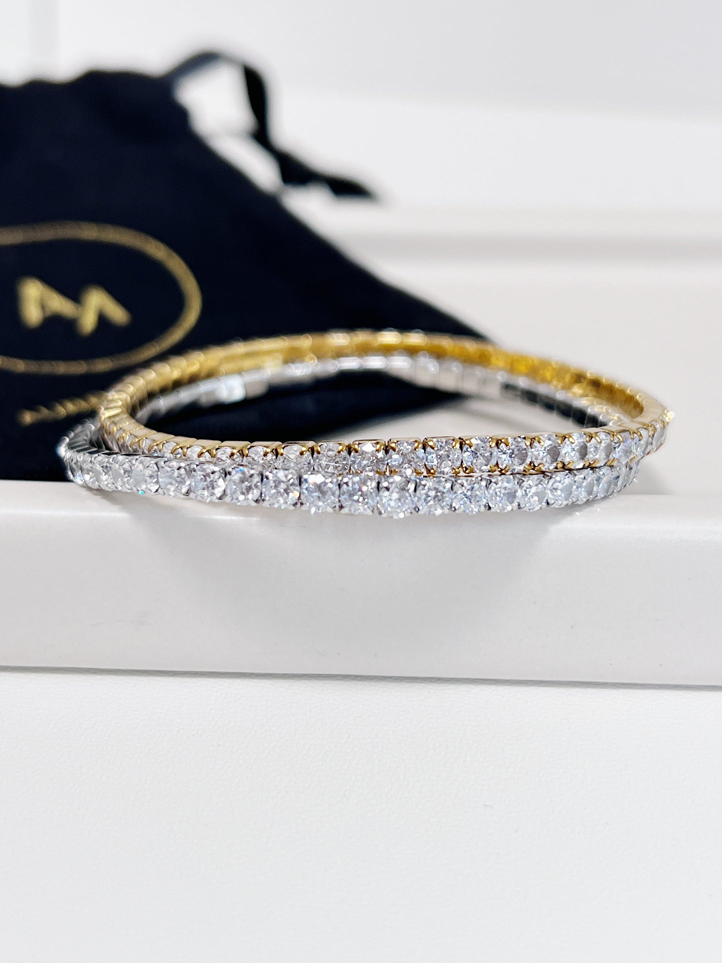 Gold and silver diamond bracelet on a white surface with a branded black drawstring bag in the background.