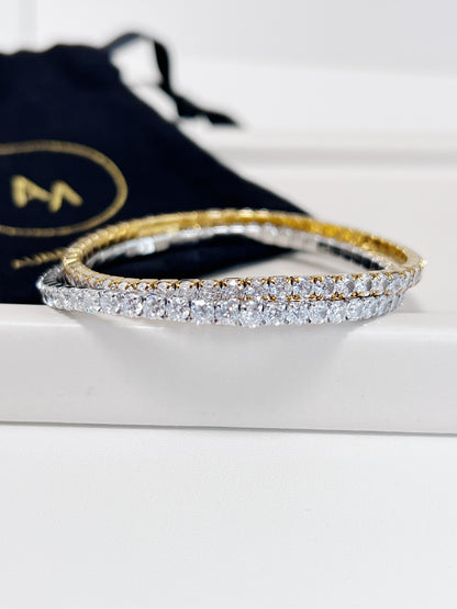 Gold and silver diamond bracelet on a white surface with a branded black drawstring bag in the background.