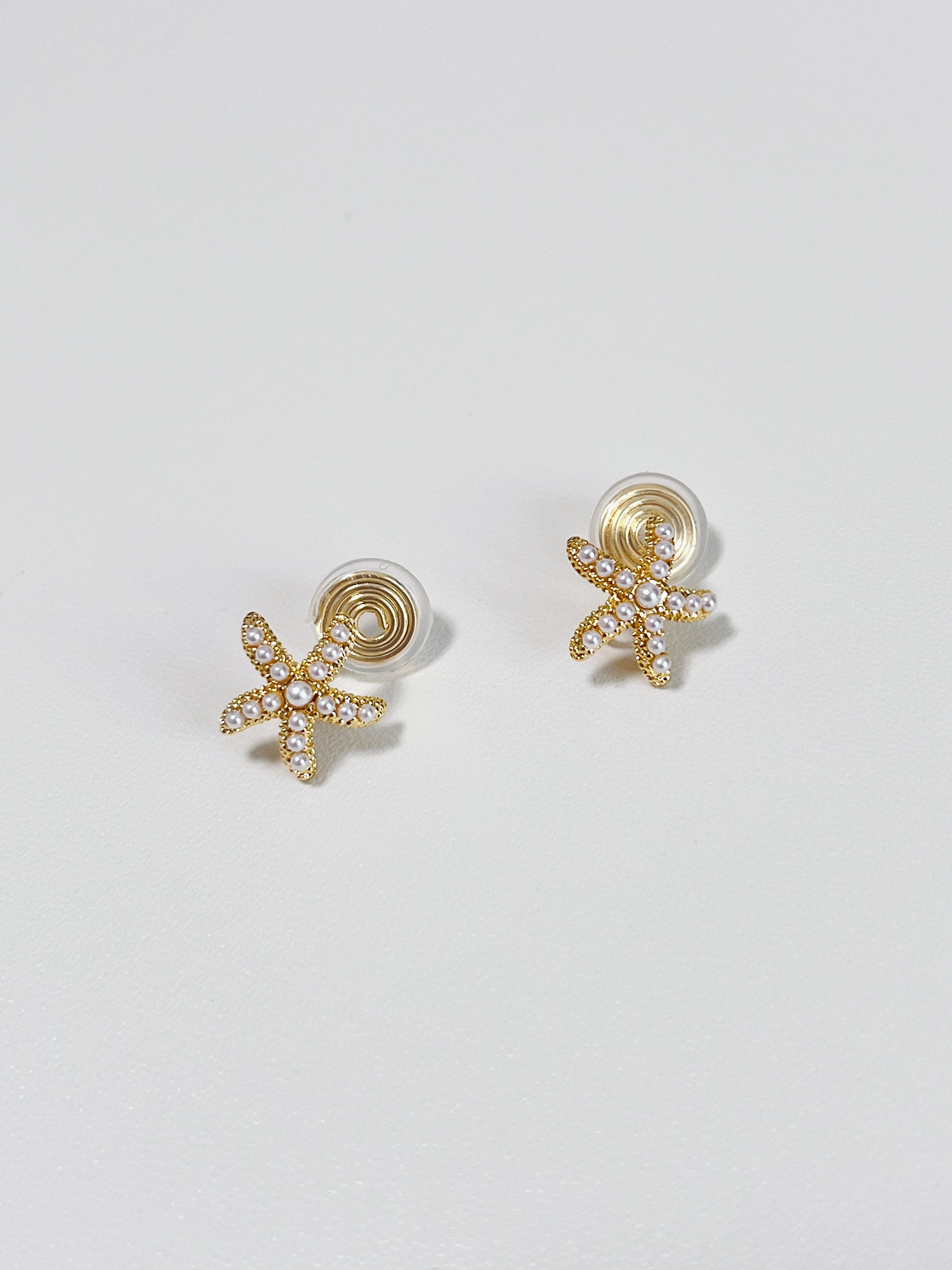 Gold starfish-shaped earrings on a light gray background