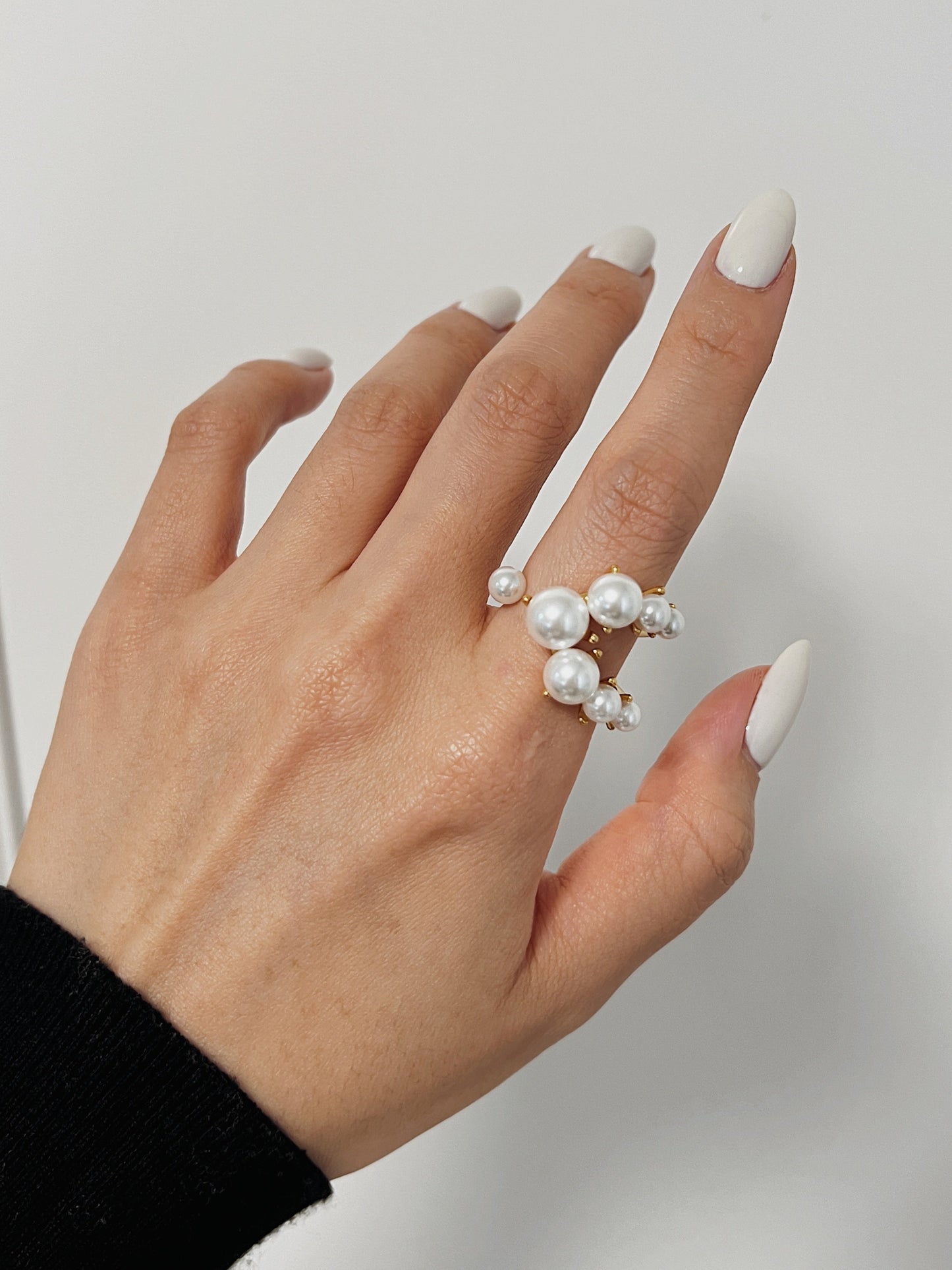 Hand wearing a pearl ring on a plain background