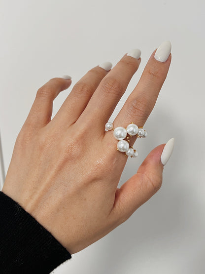 Hand wearing a pearl ring on a plain background