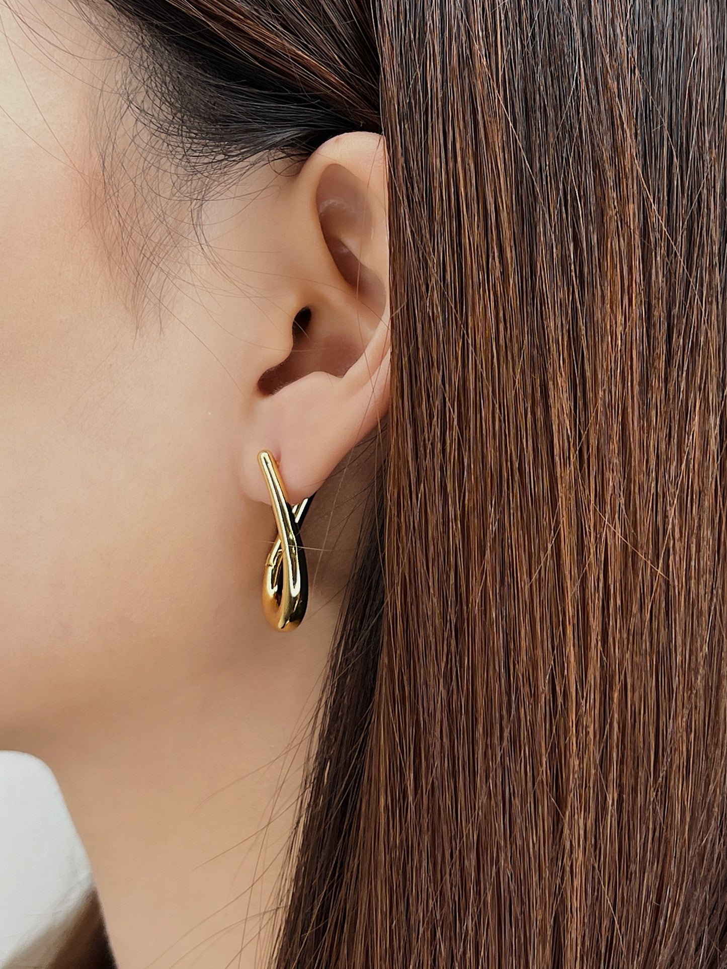 Gold irregular hoop earring worn by a person with brown hair.