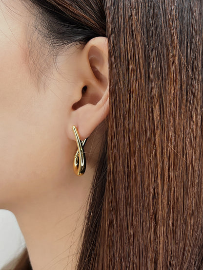 Gold irregular hoop earring worn by a person with brown hair.