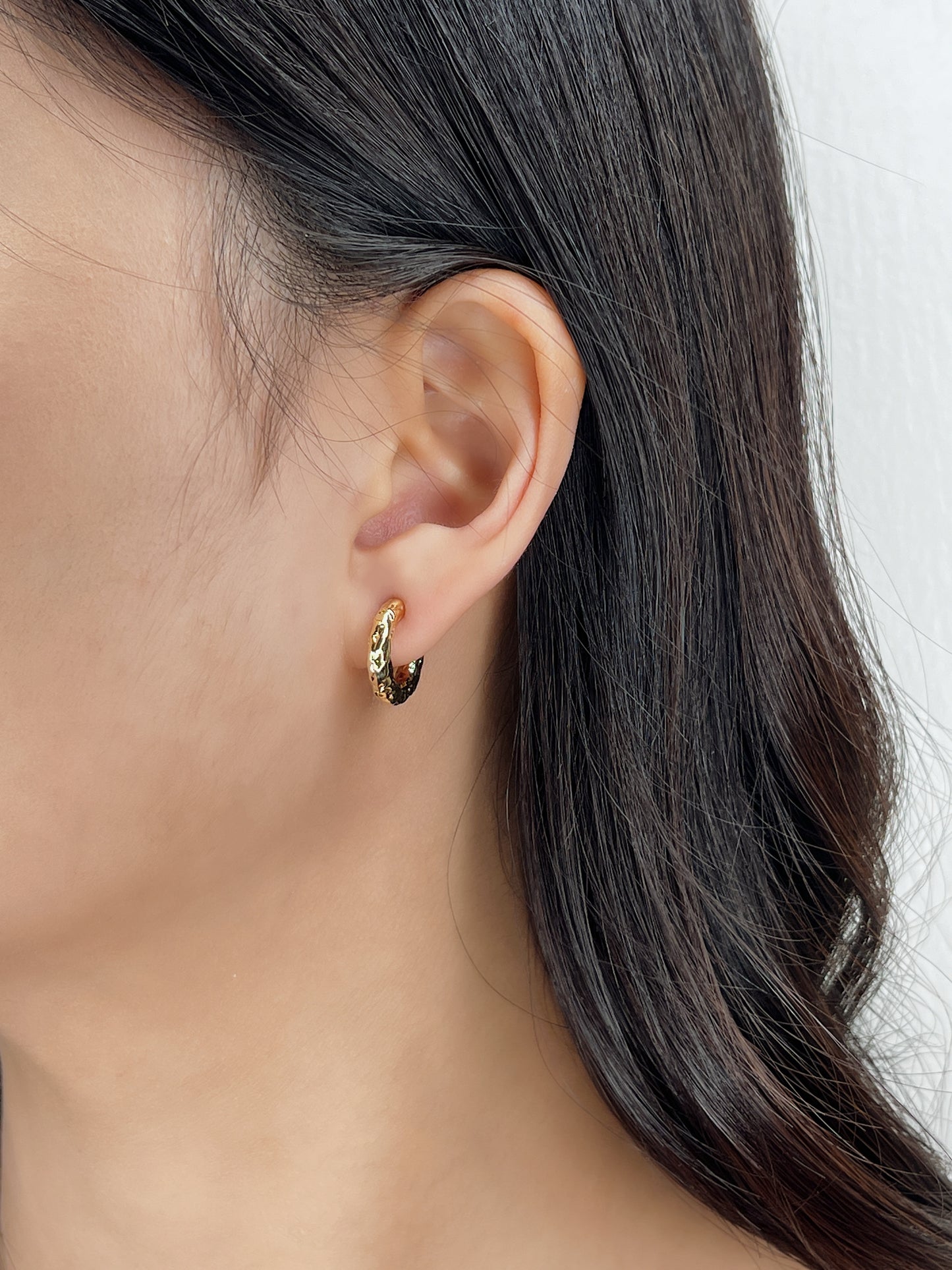 Close-up of a person wearing a gold hoop earring with a plain background