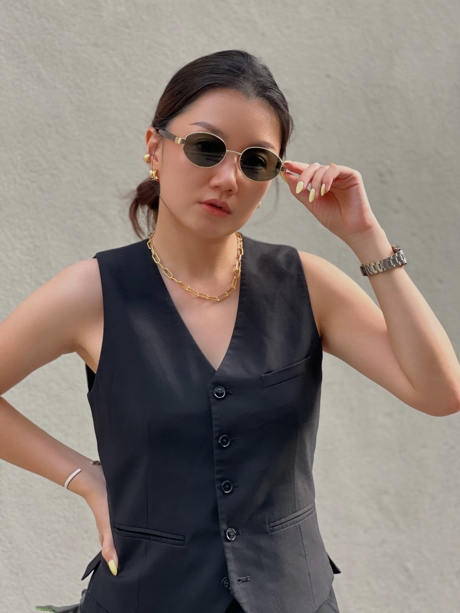 Woman wearing a black sleeveless vest top and sunglasses, layer up with gold jewelry like necklace, earrings and bangle