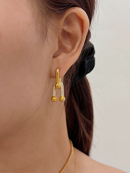 Close-up of a gold drop hoop earrings with diamond pave and u shape detail at the bottom, worn on an ear.