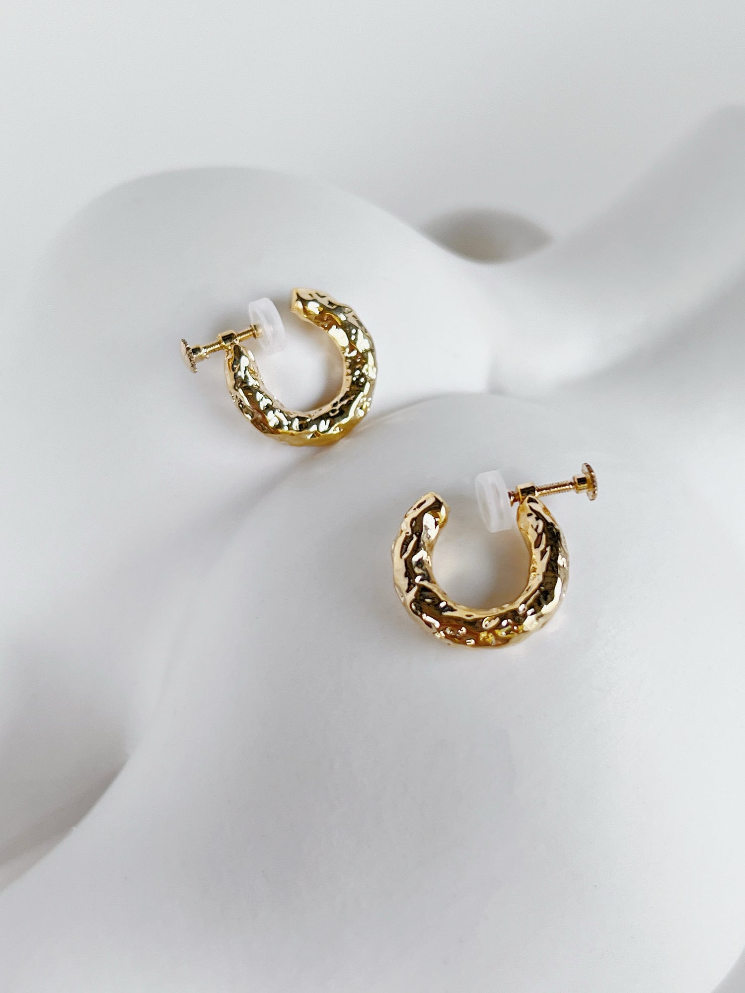 Gold hammered huggie clip on hoop earrings on a white ceramic vase surface
