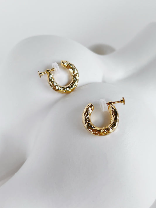 Gold hammered huggie clip on hoop earrings on a white ceramic vase surface