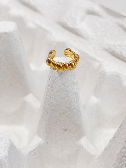 Gold ear cuff with a unique design on a textured white surface