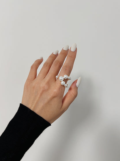 Hand wearing a pearl ring on a plain background