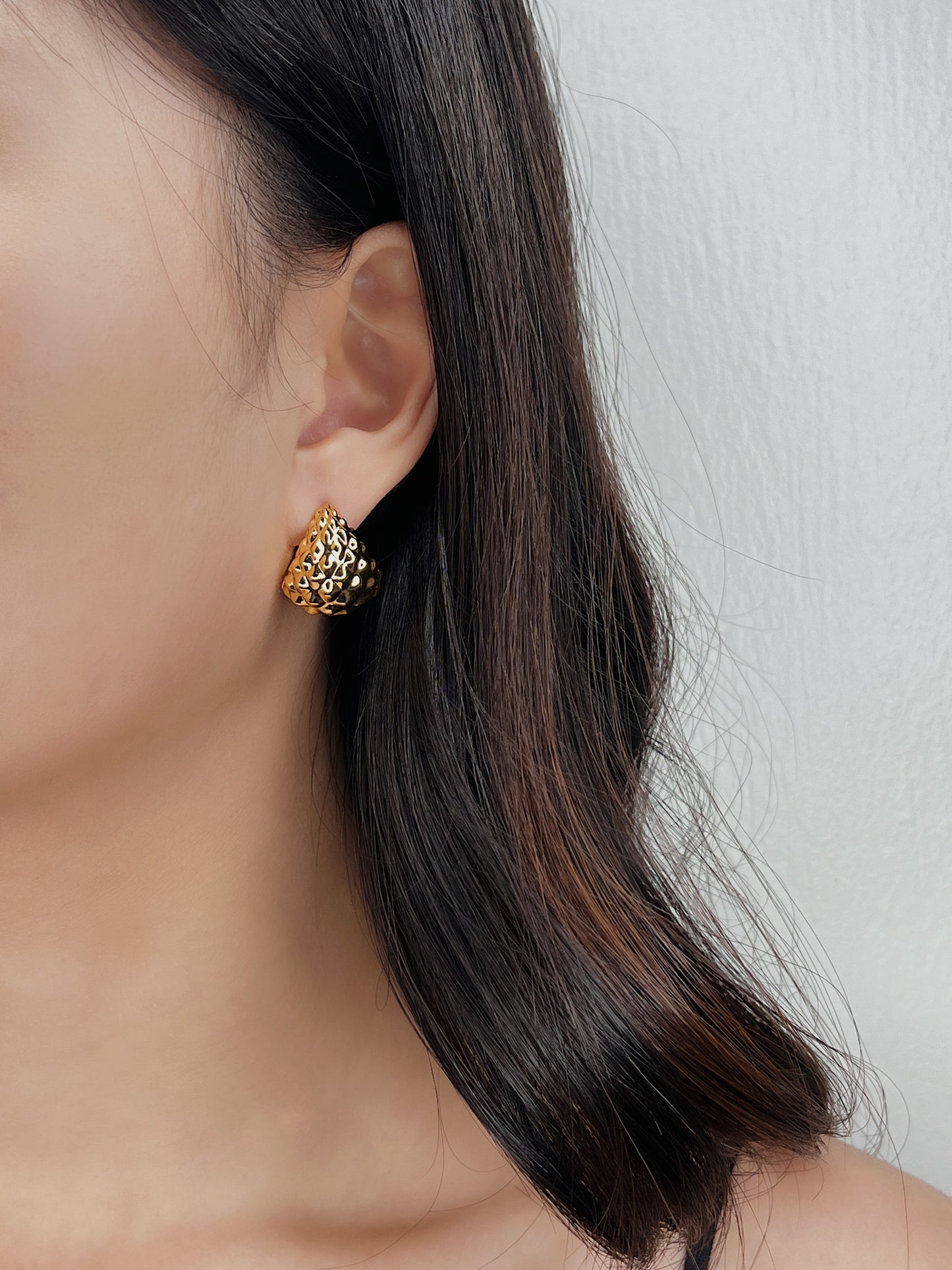 Close-up of a person wearing a gold earring with a textured design.