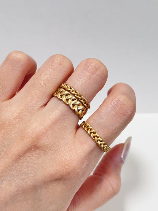 Gold braided ring on a hand against a light background
